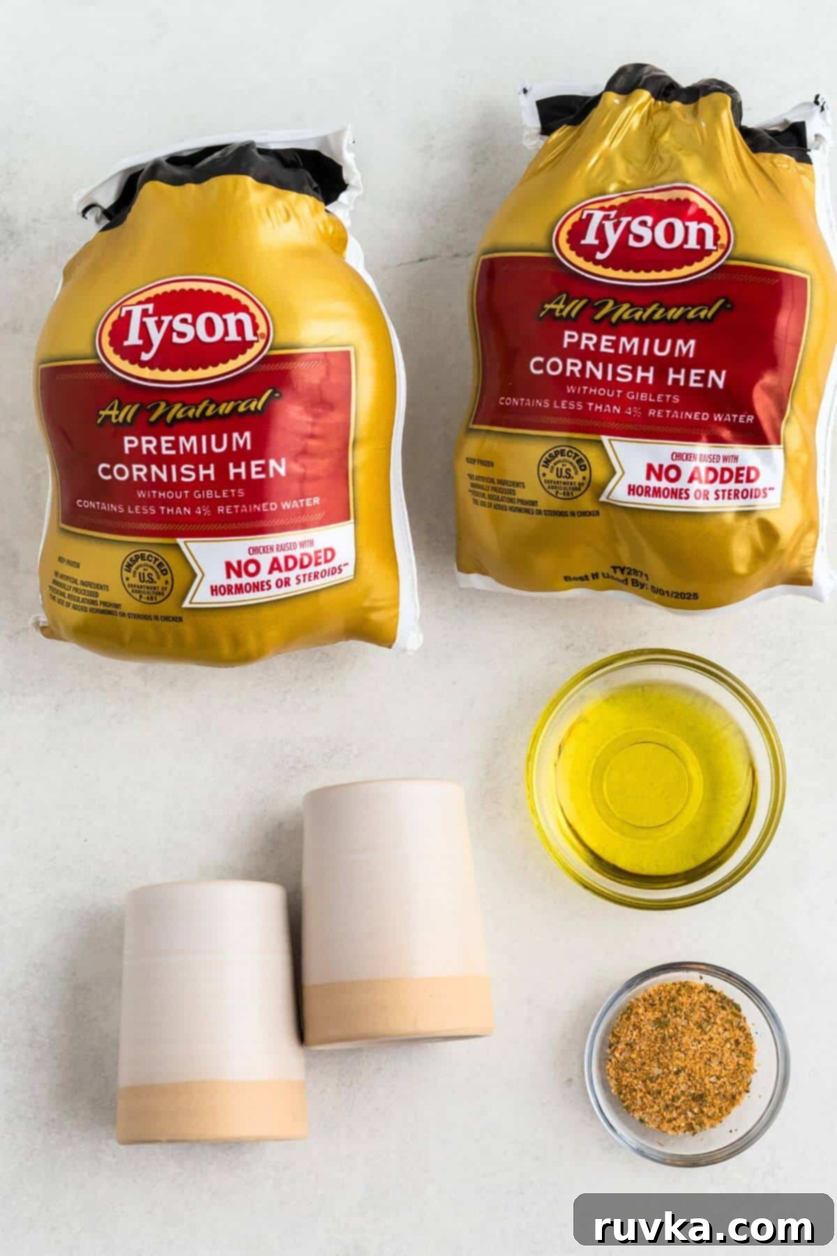 Crispy Air Fryer Cornish Game Hen 3 Ingredients of Cornish hens, olive oil, poultry seasoning and salt and pepper on a white marble table.