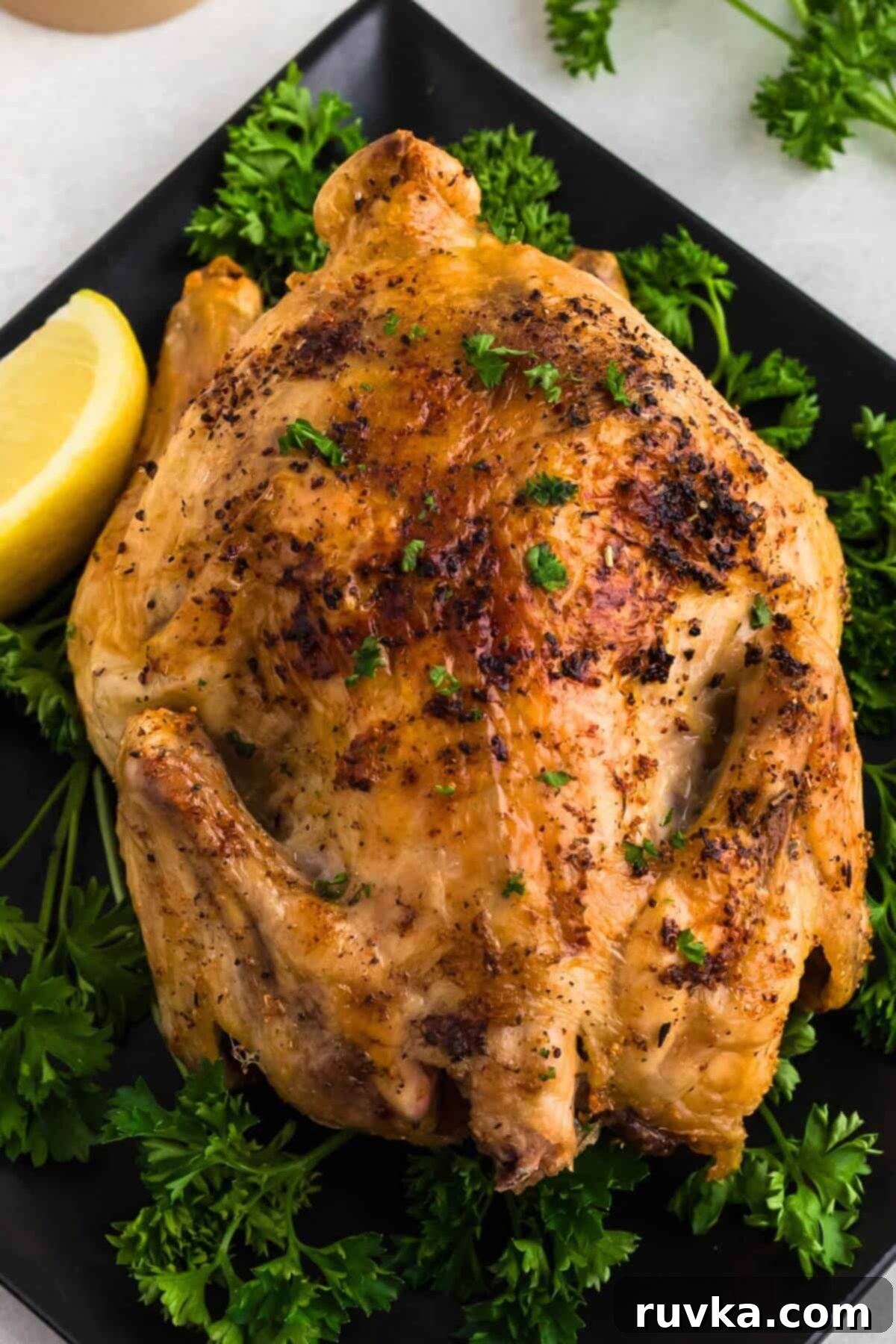 Crispy Air Fryer Cornish Game Hen 7 Juicy golden brown Cornish hen seasoned and served on a black plate then garnished with parsley and lemon wedges.