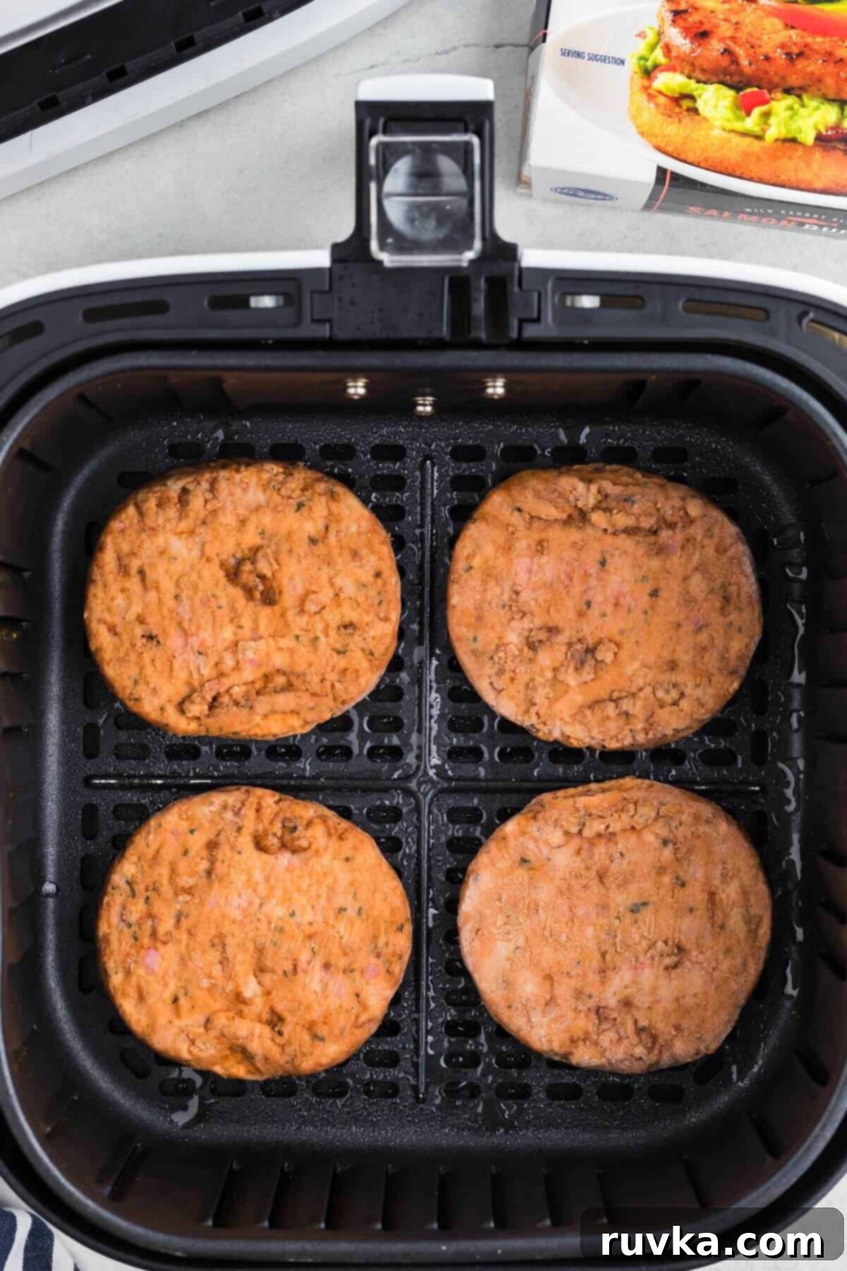 Crispy Air Fryer Frozen Salmon Burgers 4 Frozen salmon burgers in the air fryer basket before being cooked.