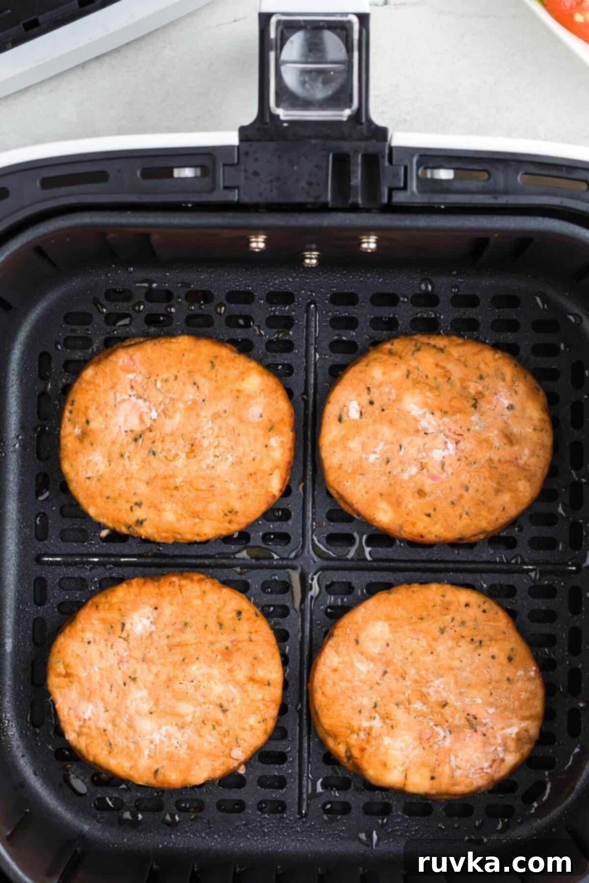 Crispy Air Fryer Frozen Salmon Burgers 5 Four pink cooked salmon patties in the air fryer basket.