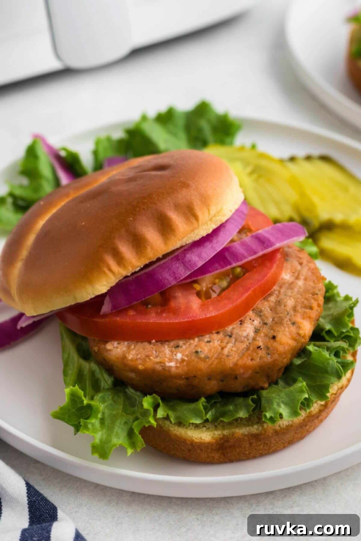 Crispy Air Fryer Frozen Salmon Burgers 6 Salmon burger on a hamburger bun with lettuce, onion, tomato, and pickles on the side.