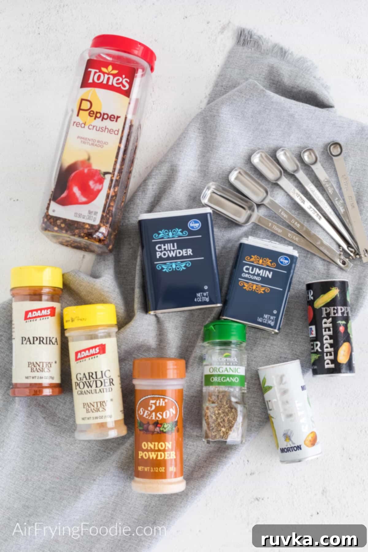 Craft Your Own Taco Spice Blend 4 White table with a greay cloth and the seasonings needed to make taco seasoning next to measuring spoons.