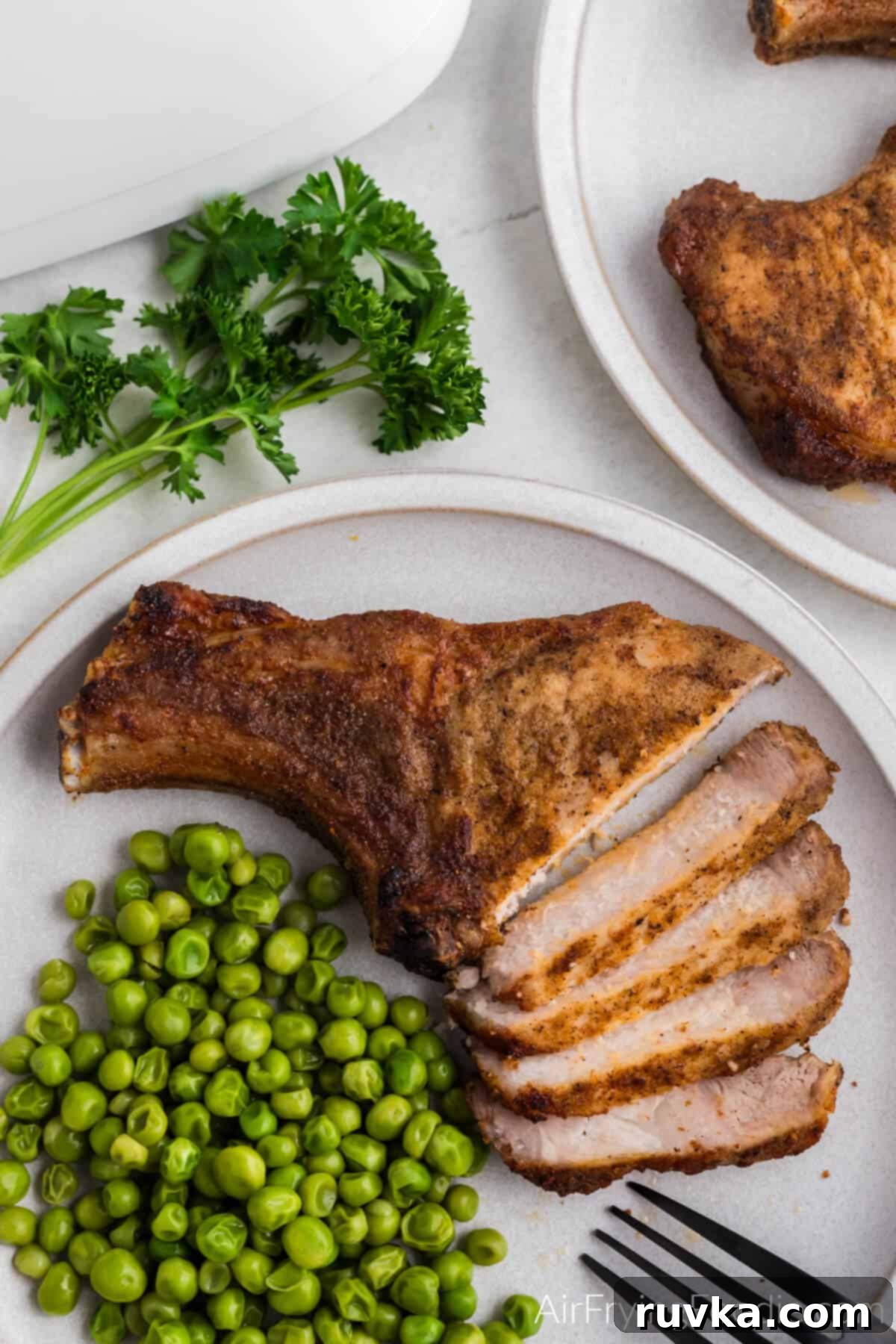 Delicious Air Fryer Pork Steaks 2 Pork steak air fried and sliced on a white plate with a side of green peas.