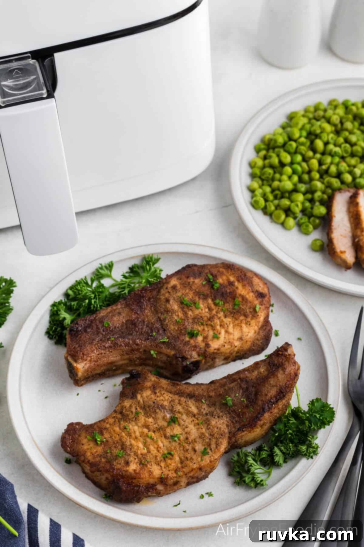 Delicious Air Fryer Pork Steaks 3 Photo of air fried pork steaks on a plate with fresh parsley on the sides.
