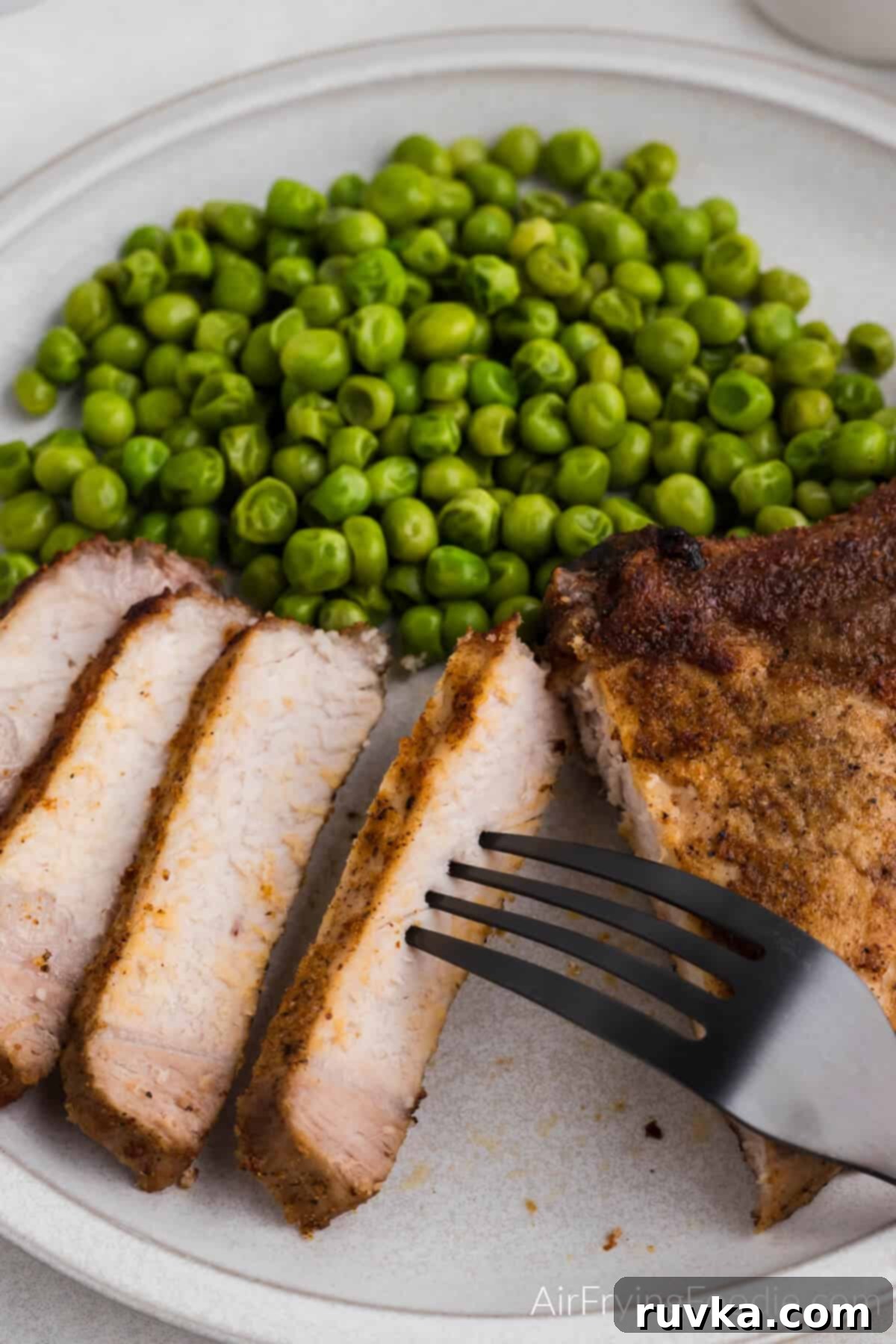 Delicious Air Fryer Pork Steaks 7 Sliced pork steak on a white plate with a side of cooked green peas.