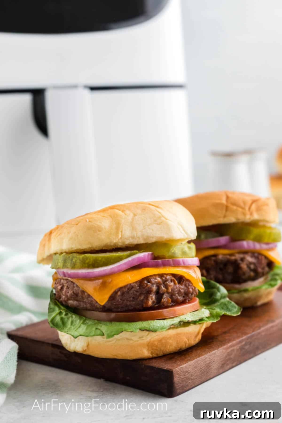 Easy Air Fryer Beyond Burger 7 Two air fried Beyond burgers on a cutting board in front of the air fryer.