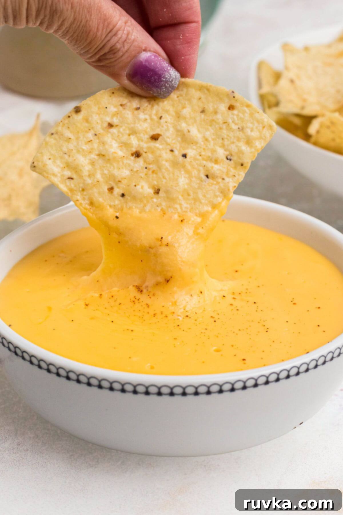 Creamy Cheese Sauce 2 Tortilla chip being dipped into melted cheese in a small white bowl.