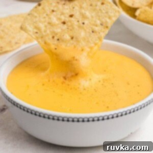 Creamy Cheese Sauce 10 Tortilla chip being dipped into melted cheese in small white bowl.