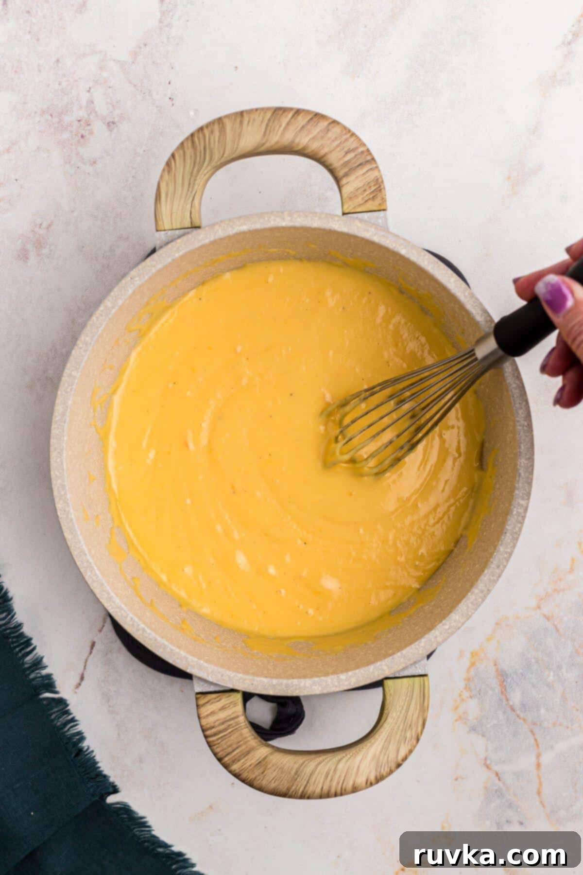 Creamy Cheese Sauce 7 Creamy cheese sauce being stirred in a sauce pan.