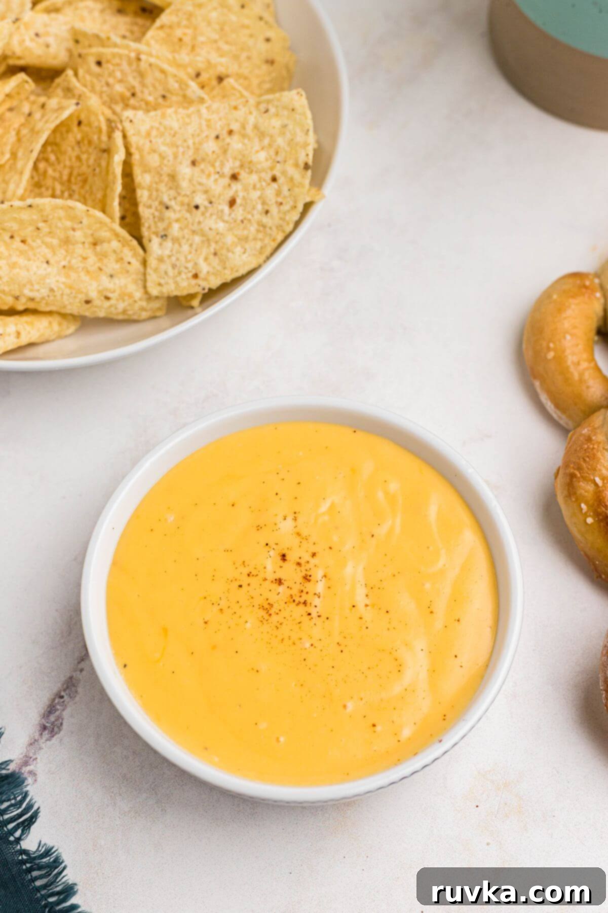Creamy Cheese Sauce 8 Creamy cheese sauce in a white bowl with chips and soft pretzels on the table.