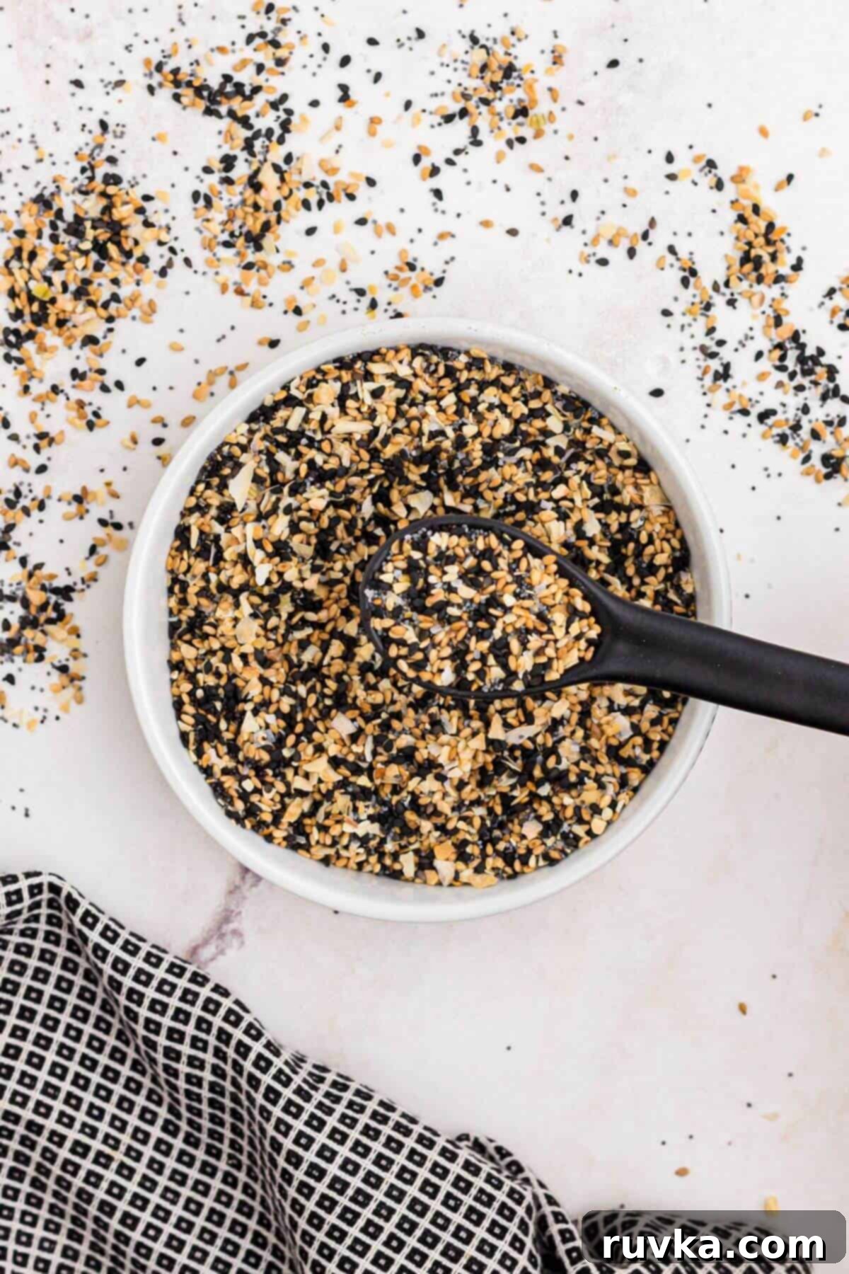 DIY Everything Bagel Seasoning 4 Seeds and seasonings in a small white bowl mixed together with a black spoon.