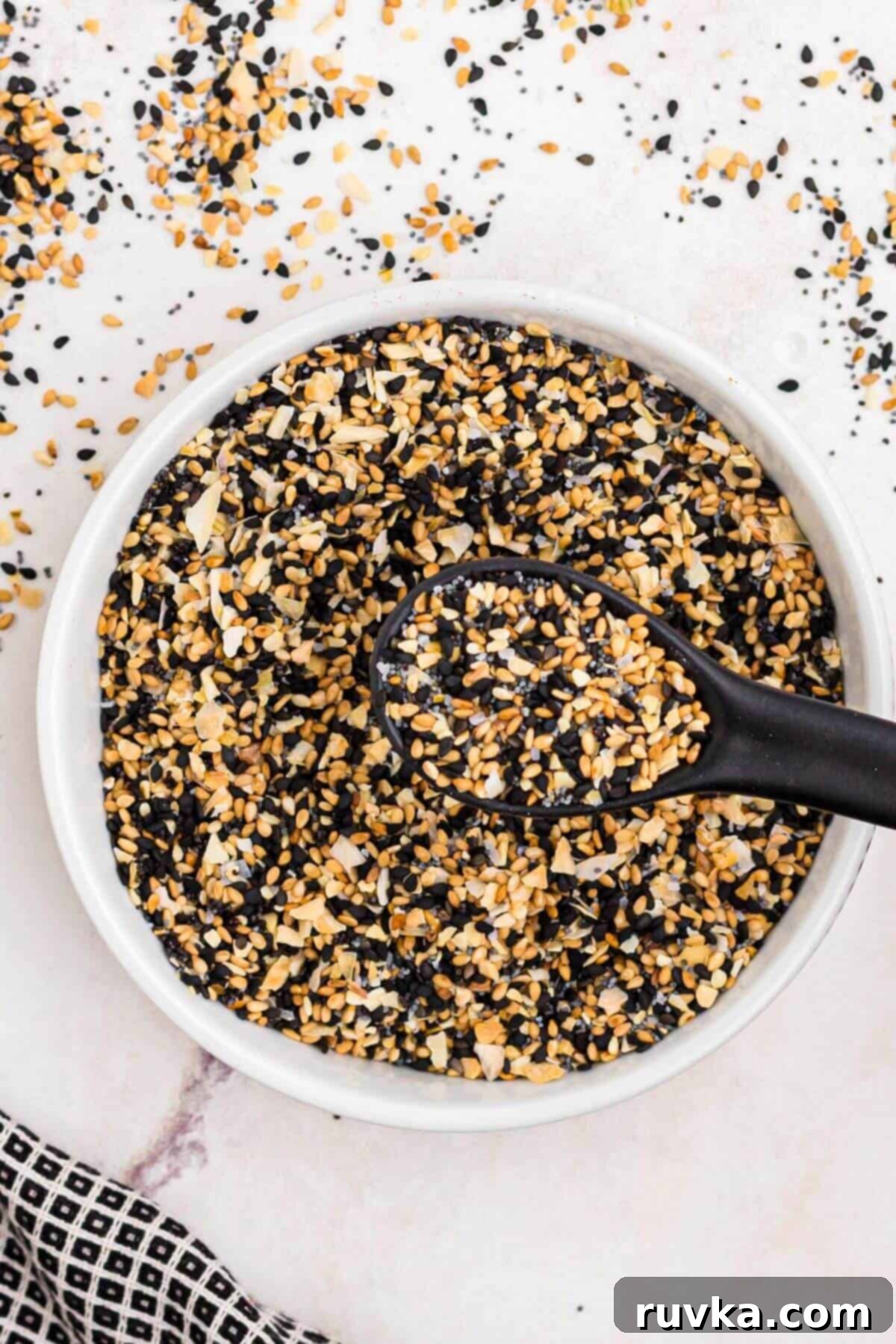 DIY Everything Bagel Seasoning 7 Seeds and seasonings in a small white bowl with a black spoon in the bowl.