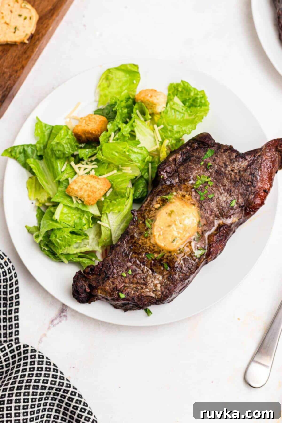 Robust Cowboy Butter 8 Steak with a slice of cowboy butter on a white plate served with a salad.