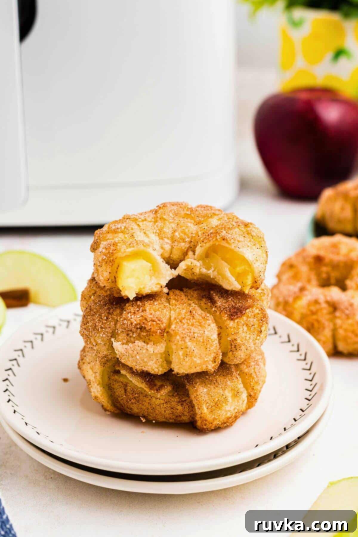Flaky Air Fryer Apple Rings 12 Golden apple rings stacked on a plate with a bite taken out of the top ring showing the inside.
