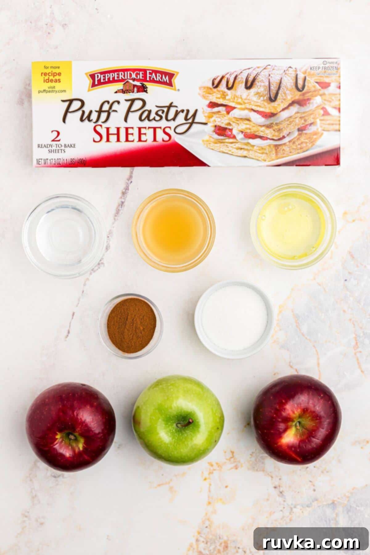 Flaky Air Fryer Apple Rings 3 Apples, puff pastry, and other ingredients needed to make apple rings on a marble table.