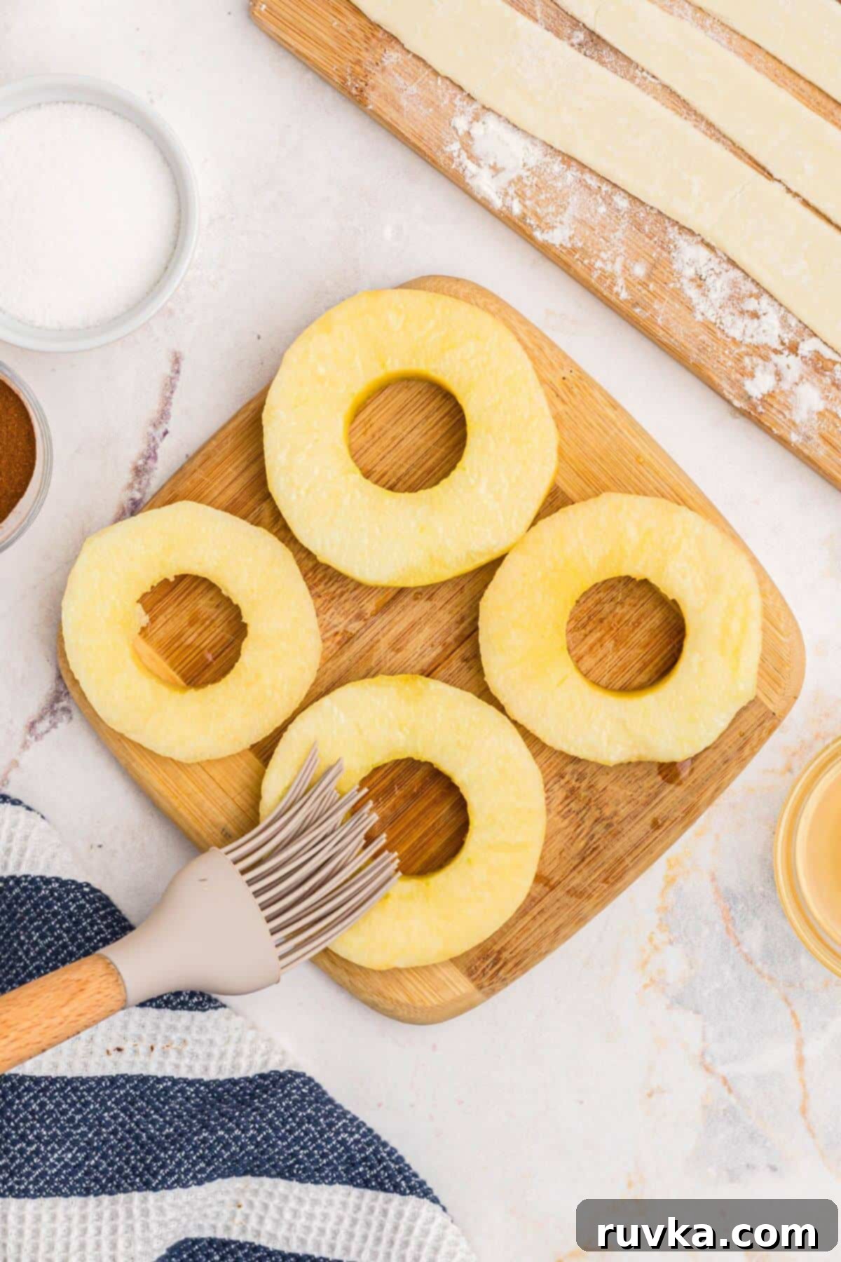 Flaky Air Fryer Apple Rings 6 Apple slices being brushed with lemon juice on a wooden cutting board.