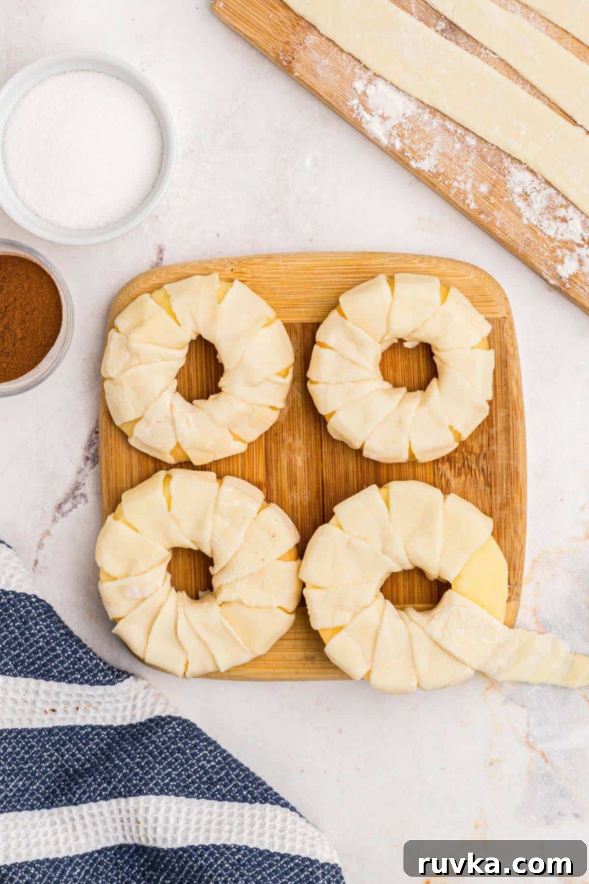 Flaky Air Fryer Apple Rings 7 Apple rings being wrapped with strips of puff pastry on a wooden cutting board.