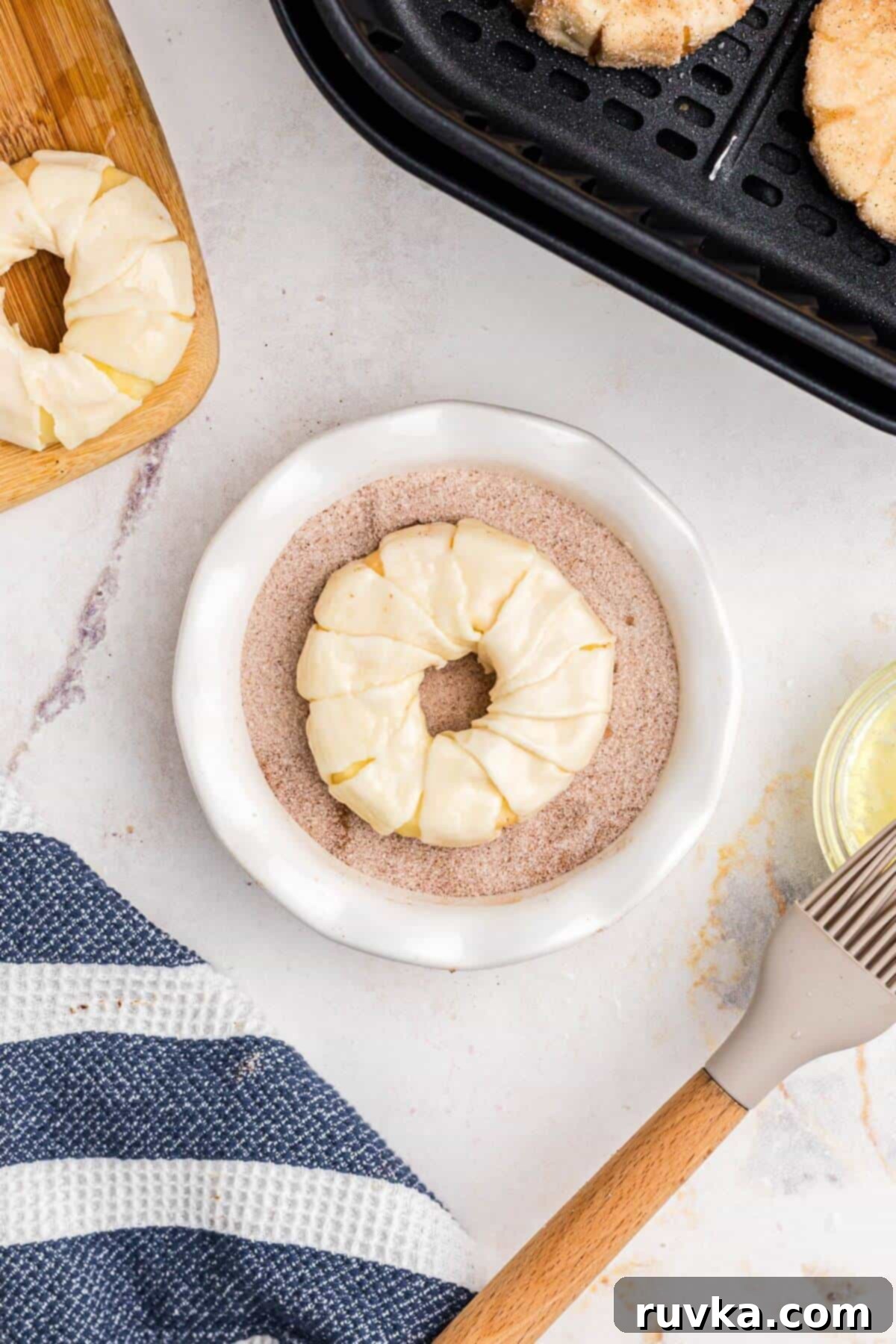 Flaky Air Fryer Apple Rings 8 Puff pastry wrapped apple rings being coated in a cinnamon sugar mixture and then placed into air fryer basket.