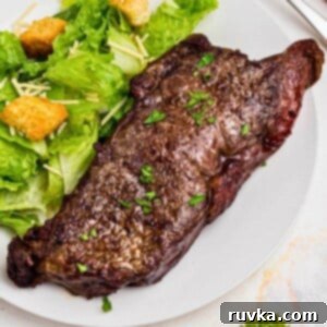 Finished Air Fryer New York Strip Steak Juicy Air Fryer New York Strip Steak served on a white plate with a side salad, ready to eat.