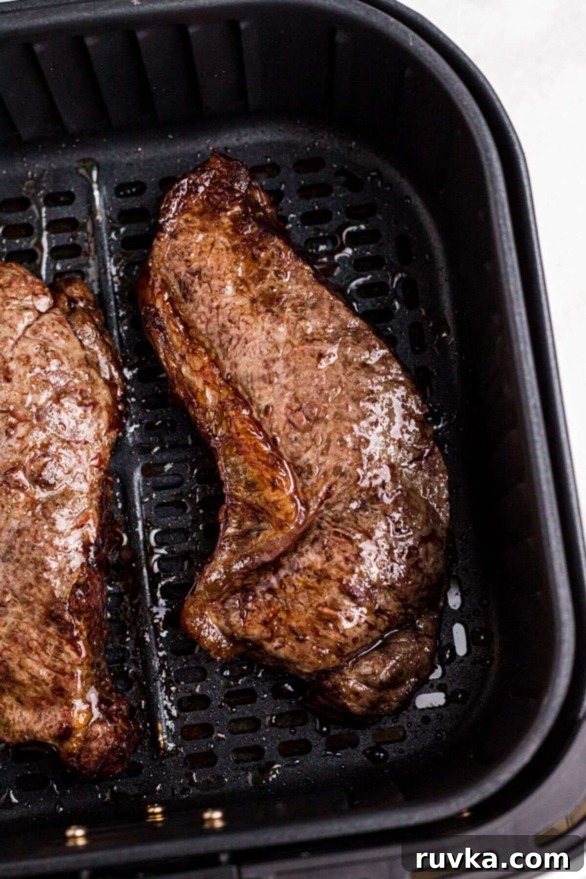 Resting Air Fried New York Strip Steak Two perfectly cooked, juicy New York strip steaks resting in the air fryer basket after cooking.