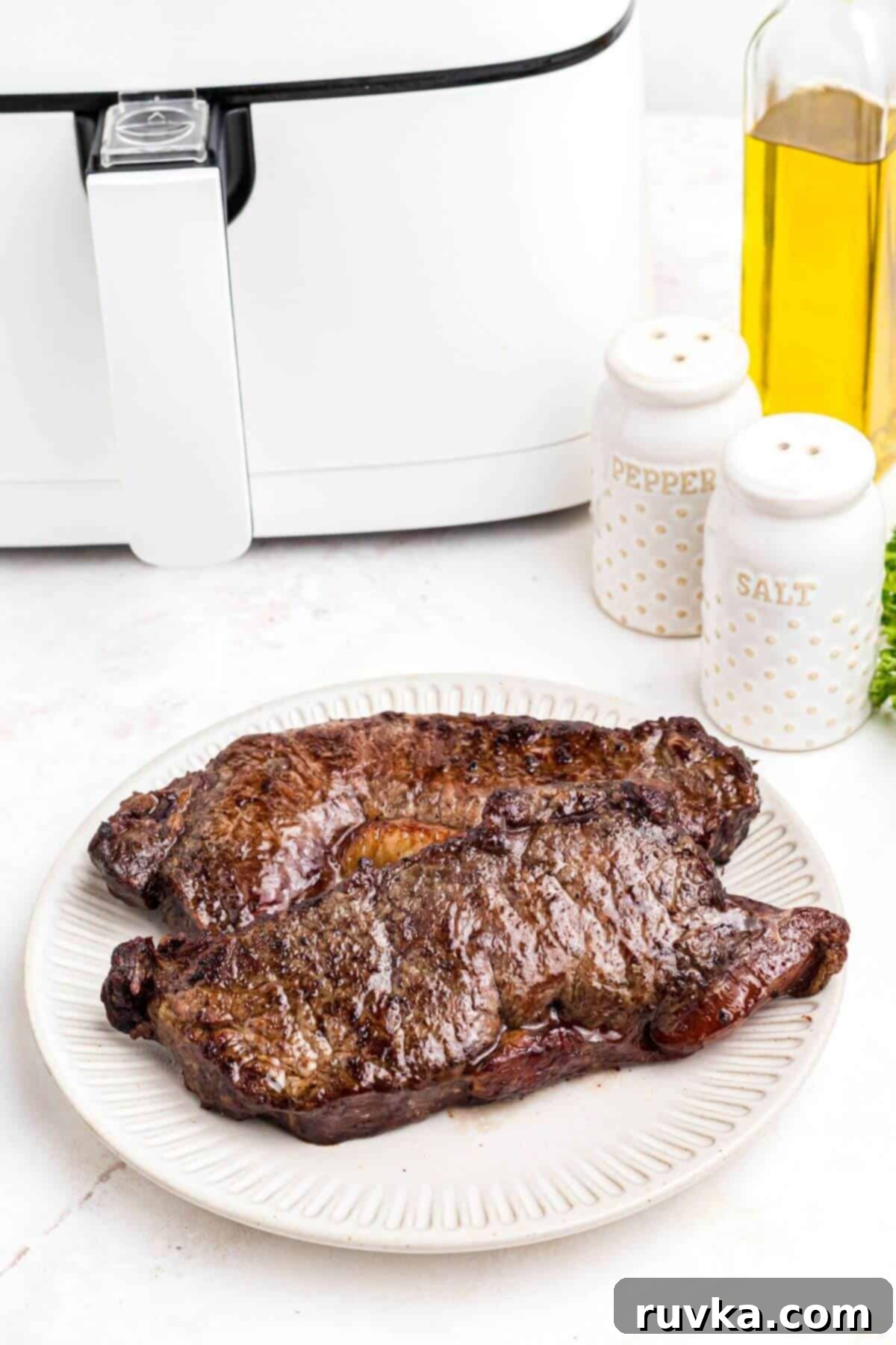 Cooked Air Fryer New York Strip Steak Slice of juicy air fried New York strip steak served on a white plate with a side salad.