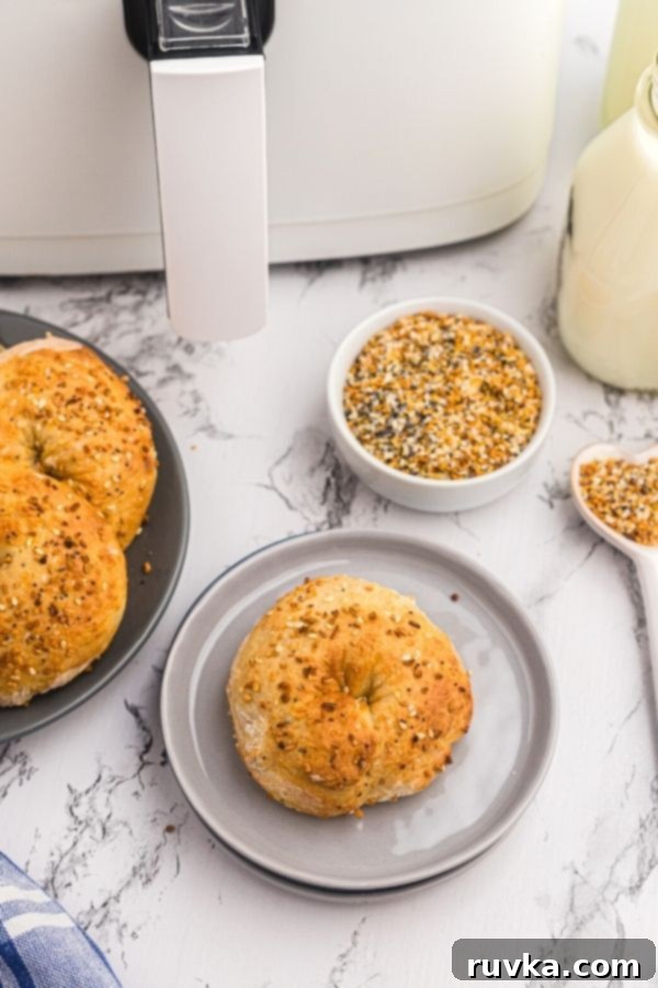 Easy Air Fryer Two-Ingredient Bagels 3 Golden bagel served on a light gray plate on a marble table. Topped with seasonings.