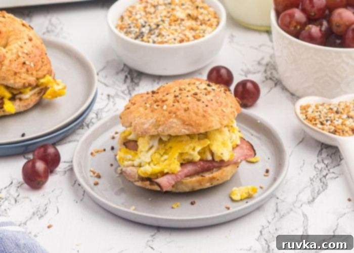 Easy Air Fryer Two-Ingredient Bagels 7 Air fryer bagel served with ham and eggs on a light gray plate on a marble table. Grapes scattered around the table.