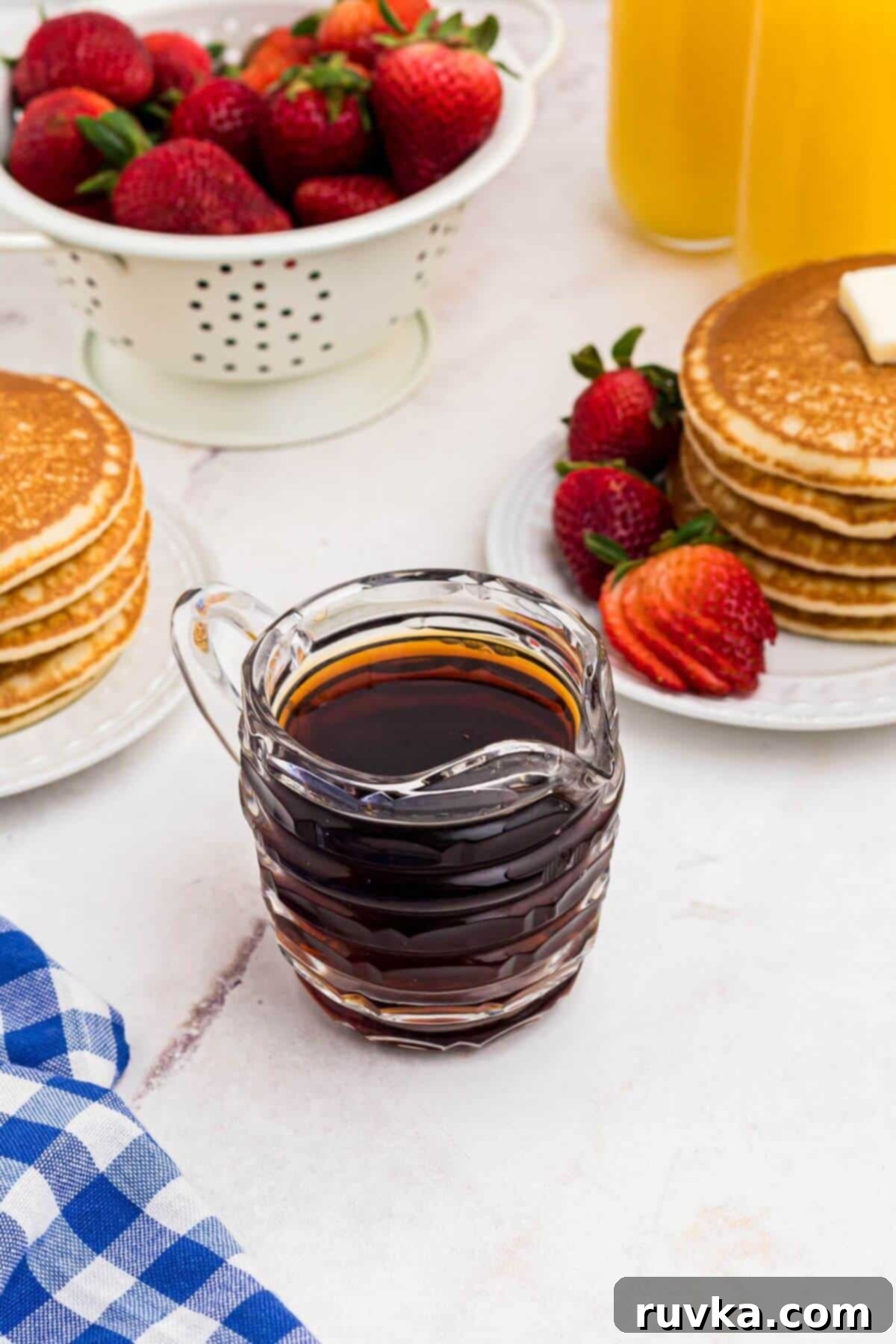 Easy Homemade Pancake Syrup 2 Small glass serving pitcher filled with homemade syrup in front of plates with stacks of pancakes and strawberries.
