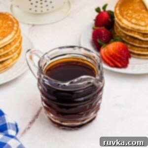 Easy Homemade Pancake Syrup 8 Homemade syrup in a glass pitcher in front of stacks of pancakes with strawberries.