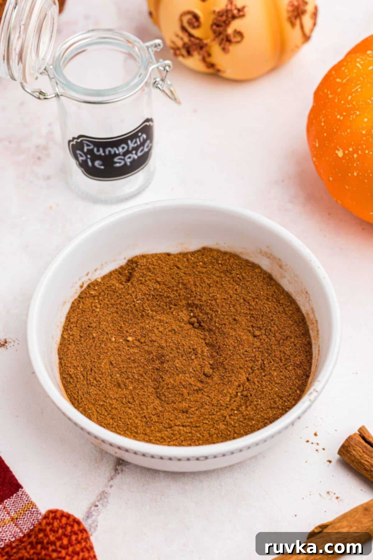Autumn Spice Blend 2 Pumpkin pie spice mixed and in a small white bowl in front of cinnamon sticks.