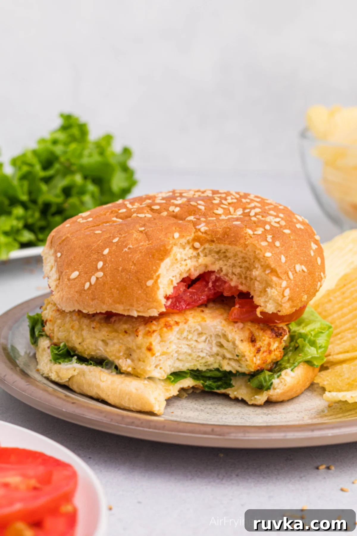 Elevate Your Burger Game: 5 Air Fryer Creations 3 An air fryer chicken burger with a bite missing, presented on a pristine white plate, showcasing its juicy interior.