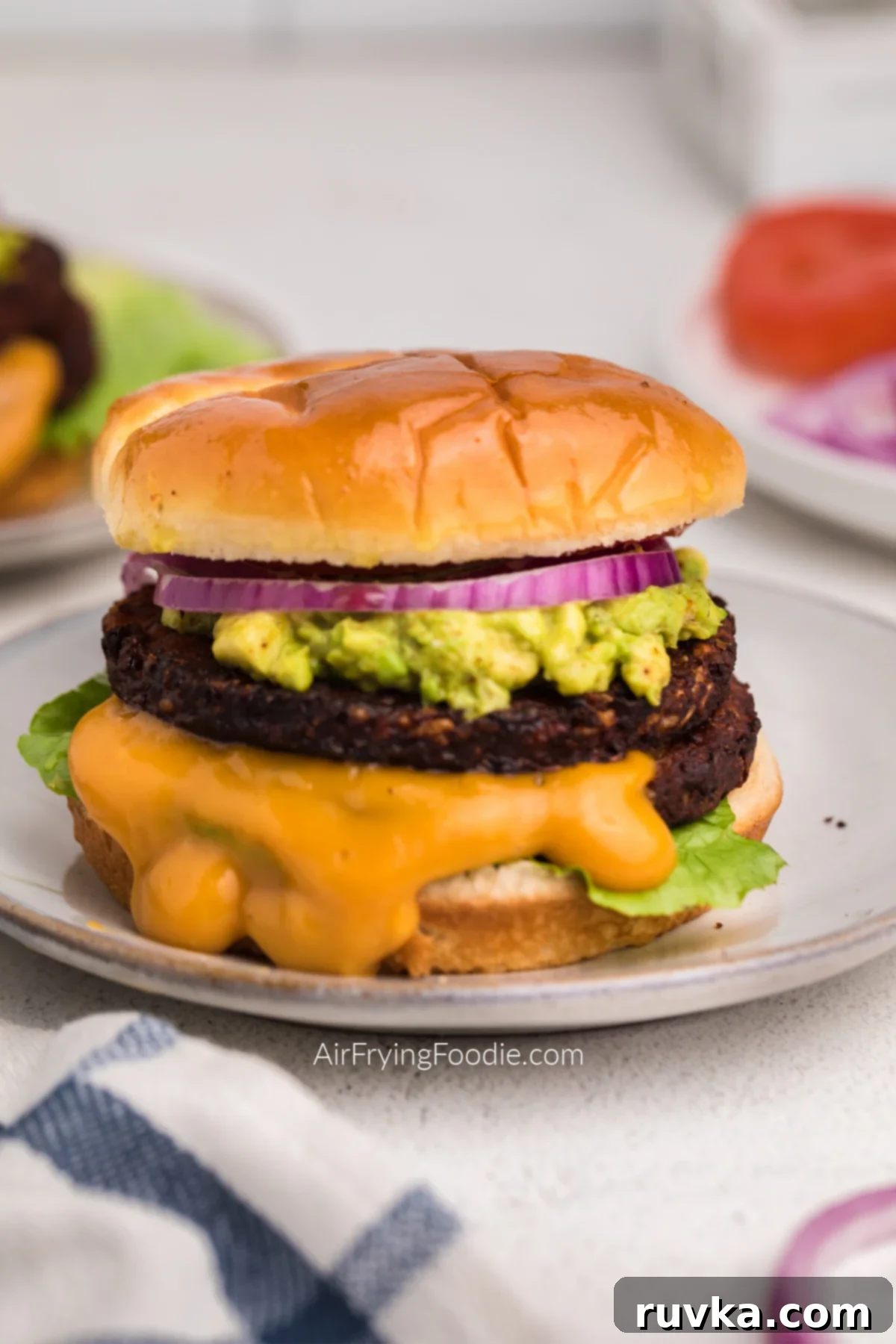 Elevate Your Burger Game: 5 Air Fryer Creations 5 A close-up shot of a gourmet black bean burger on a bun, adorned with crisp lettuce, creamy mashed avocado, sliced red onion, ripe tomato, and a drizzle of a savory sauce.