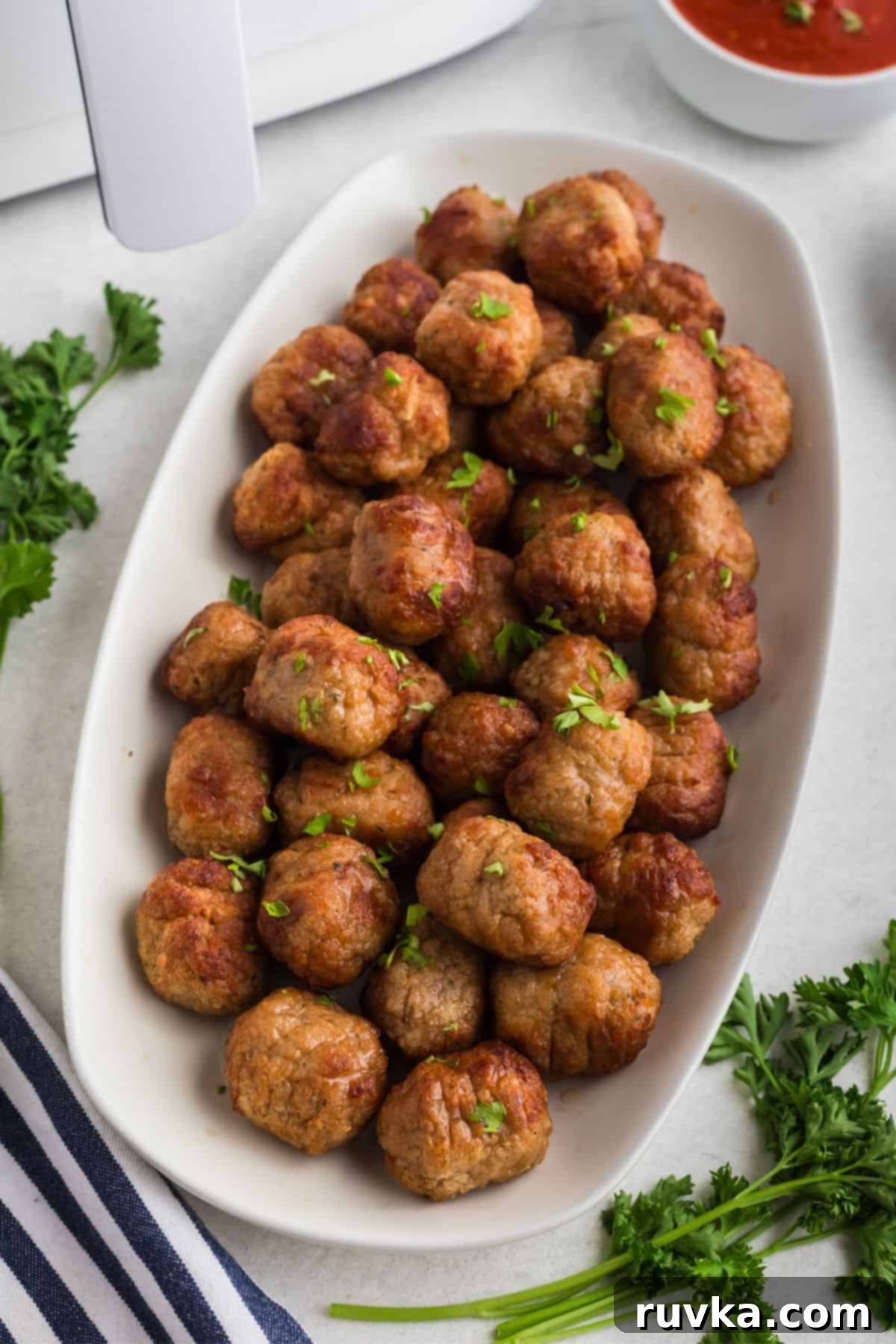 Quick Air Fryer Frozen Meatballs 2 Juicy golden brown meatballs stacked on a white plate in front of an air fryer after being cooked.