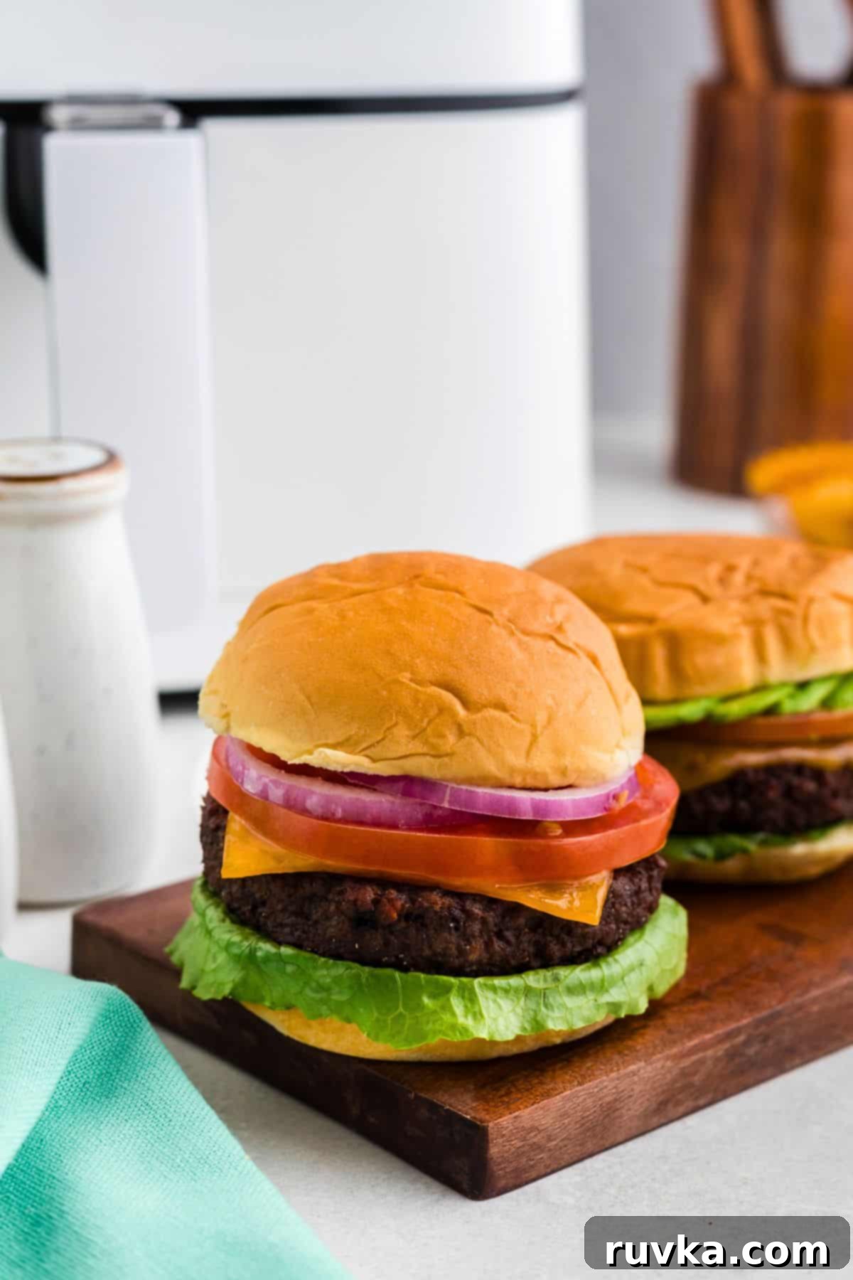 Crispy Air Fryer Impossible Burgers 2 Delicious Impossible burger in a soft bun with fresh lettuce, sliced tomatoes, and onions, served hot in front of an air fryer.