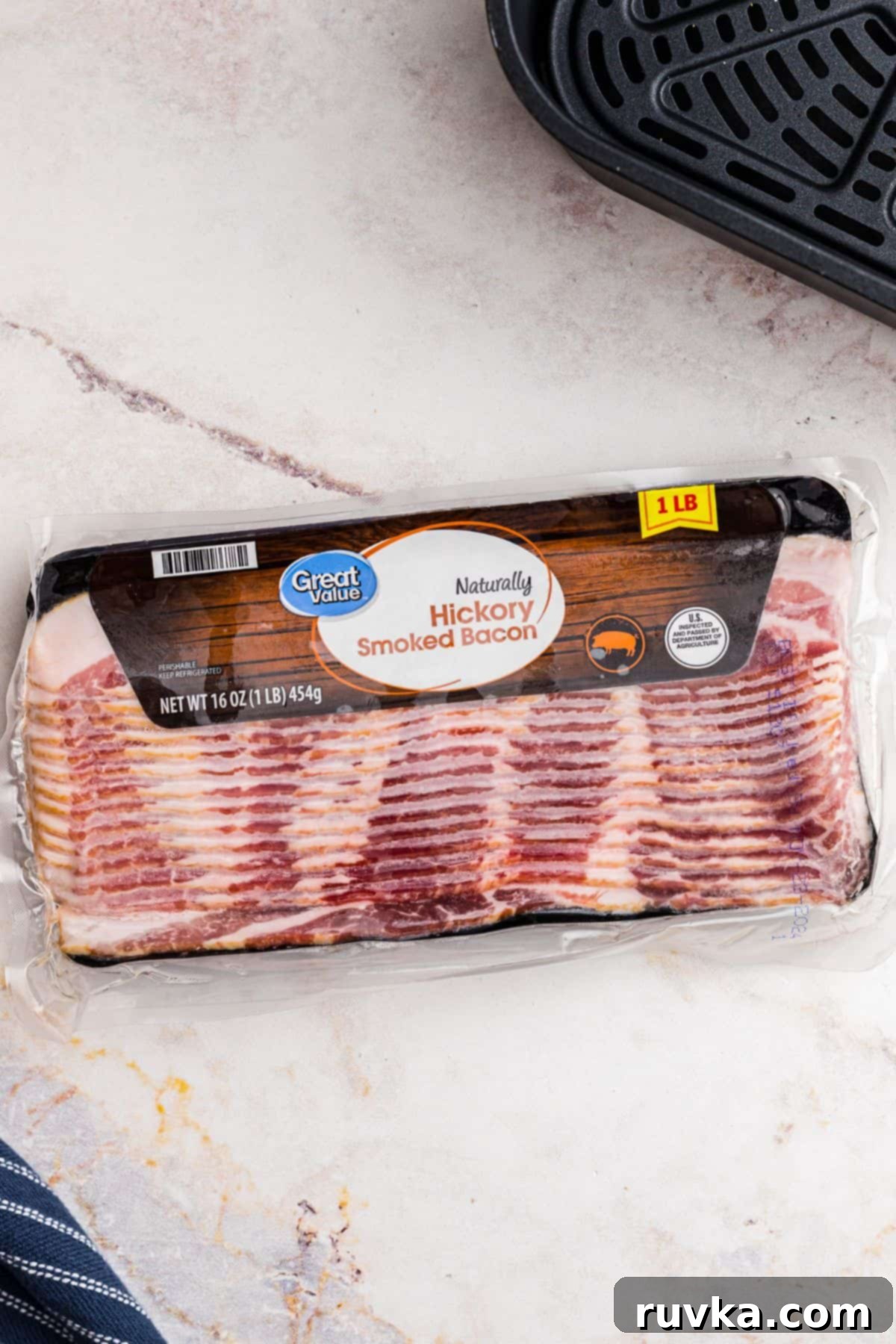 Air Fryer Frozen Bacon Hack 3 One pound package of frozen bacon in packaging, in front of air fryer basket.