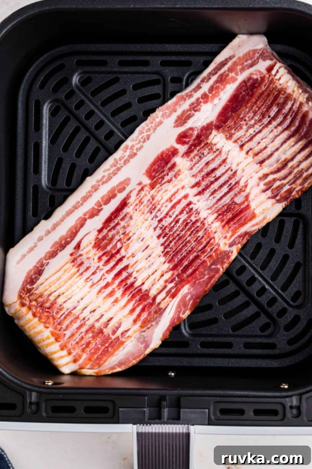 Air Fryer Frozen Bacon Hack 4 Uncooked frozen bacon strips out of packaging in the air fryer basket.