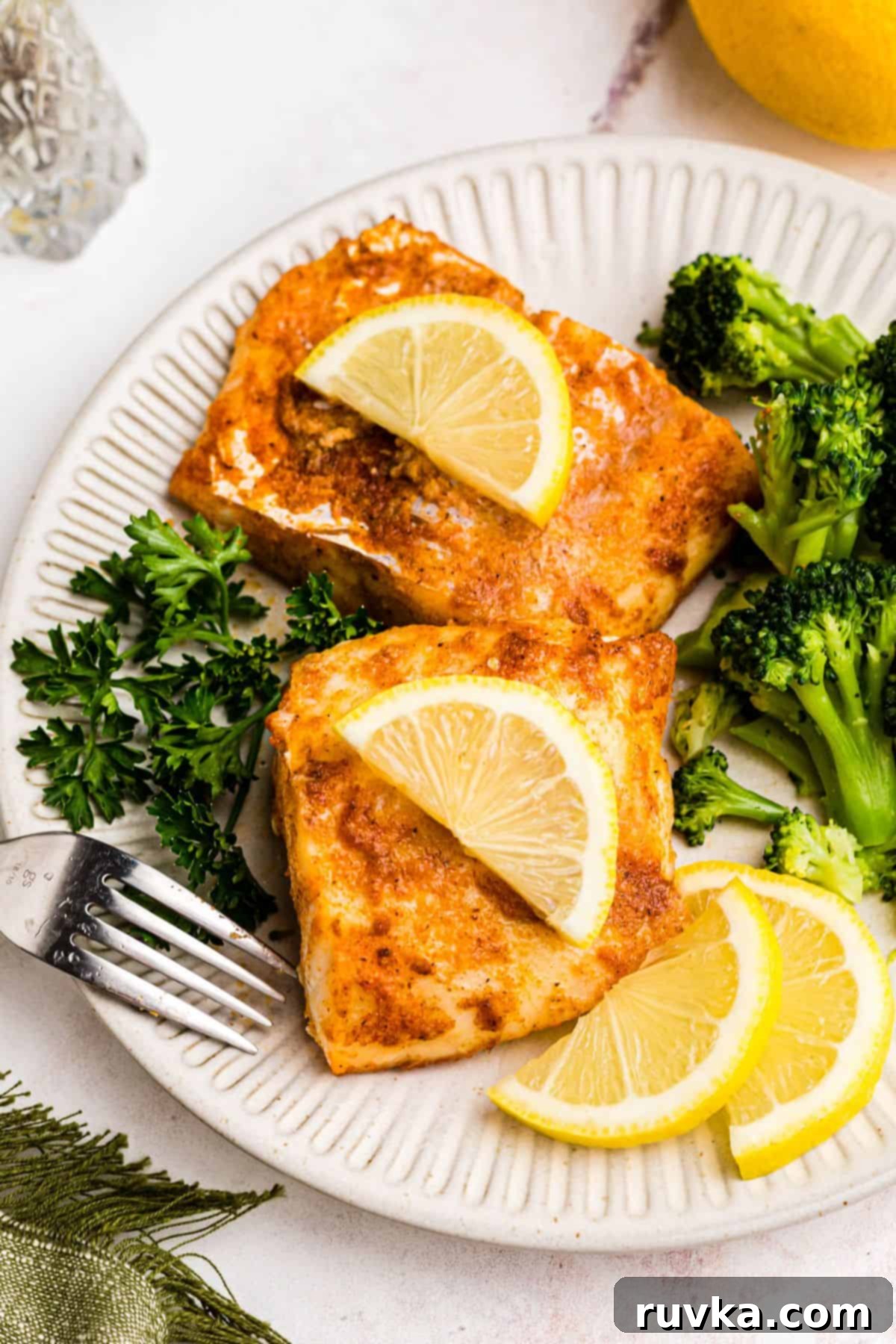 Perfect Air Fryer Frozen Cod 2 Moist air fried cod on a white plate with broccoli and lemon slices.