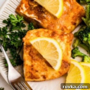 Perfect Air Fryer Frozen Cod 9 Juicy seasoned cod on a white plate, served with broccoli and lemon slices.