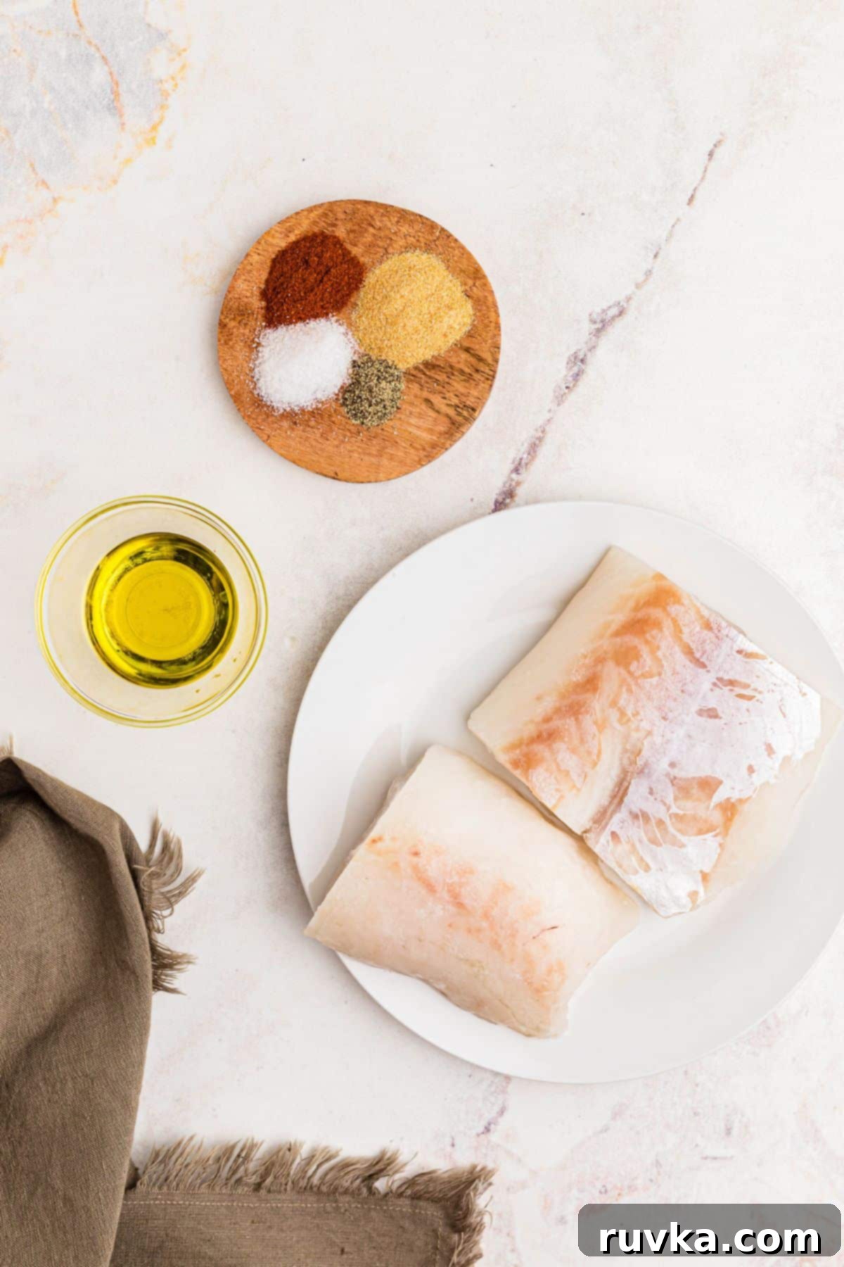 Perfect Air Fryer Frozen Cod 3 Ingredients measured out on a white marble table along with frozen cod.