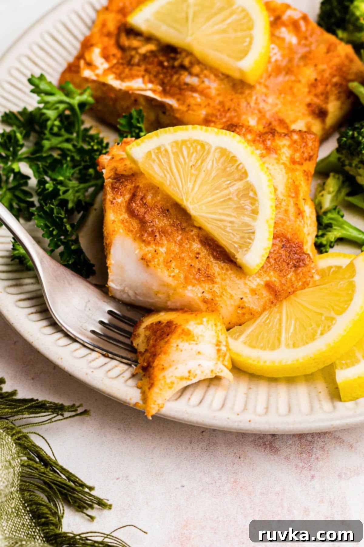 Perfect Air Fryer Frozen Cod 7 Juicy cod filet on a white plate with a lemon slice and a small piece on a fork.