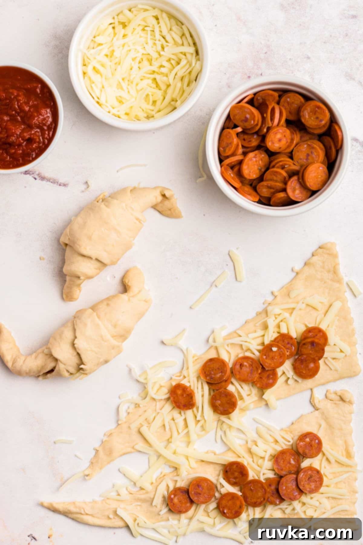 Air Fryer Pizza Crescent Bites 4 Unrolled crescent rolls with shredded cheese and mini pepperoni on top, with some already rolled into crescents.