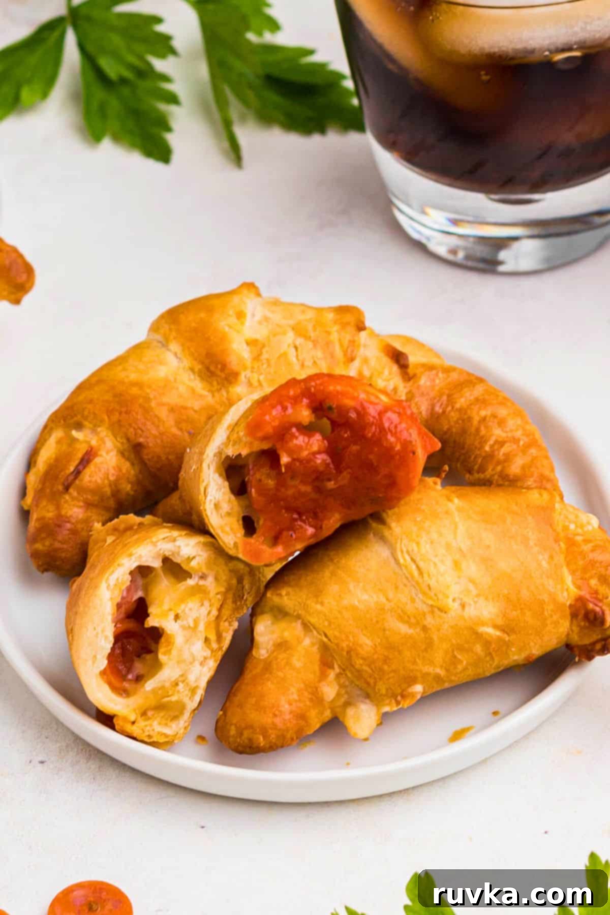 Air Fryer Pizza Crescent Bites 8 Pizza crescent rolls on a small white plate with one split open and dipped into pizza sauce, showing the gooey cheese and pepperoni inside.