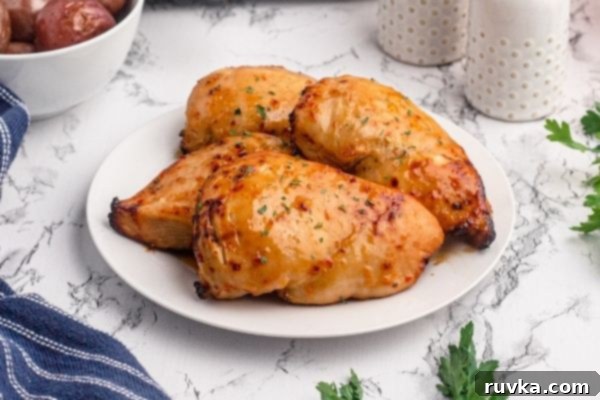 Golden Peach Air Fryer Chicken 2 Golden glazed chicken breasts, on a white plate sprinkled with dried parsley on a marble table.