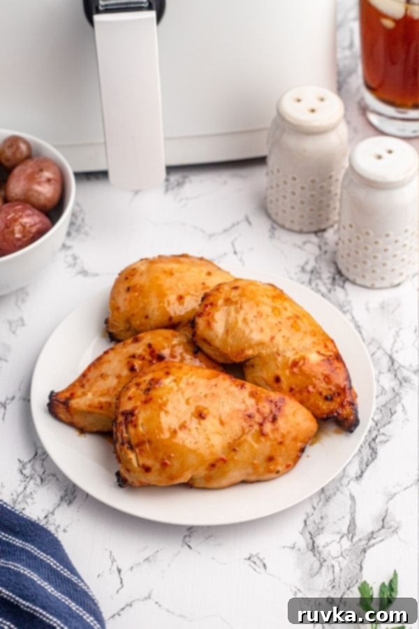 Golden Peach Air Fryer Chicken 3 Golden chicken breasts in front of an air fryer served on a white plate.