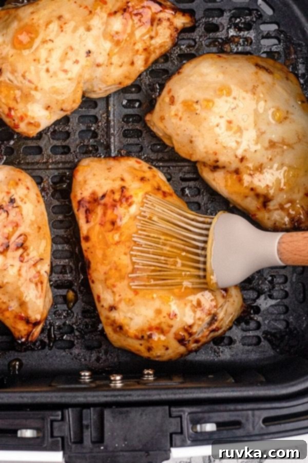 Golden Peach Air Fryer Chicken 7 Chicken in the air fryer basket being brushed with peach glaze.