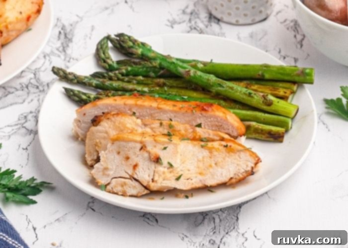 Golden Peach Air Fryer Chicken 9 Sliced chicken breast served on a white plate with green asparagus.