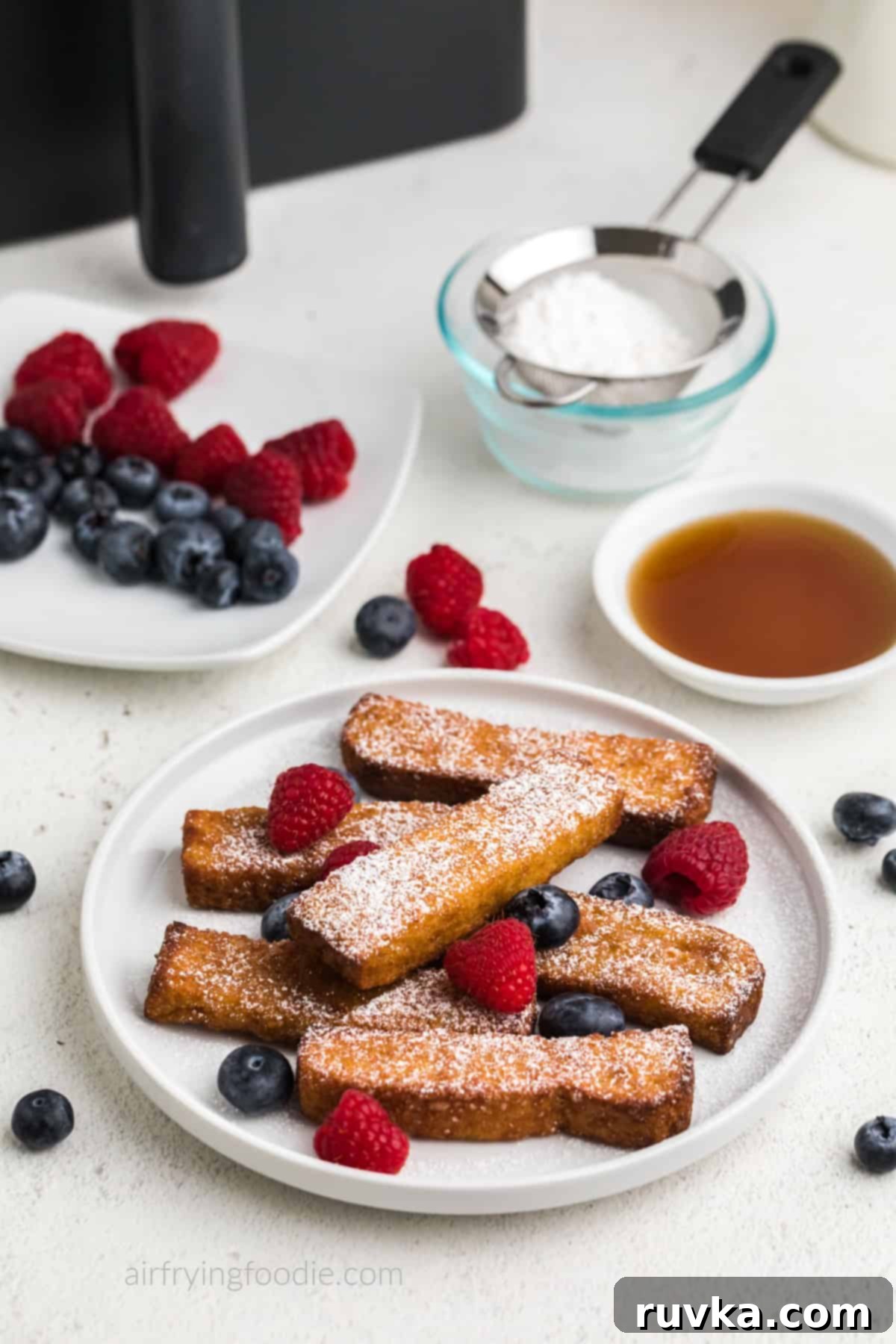 Crispy Air Fryer Frozen French Toast Sticks 2 Air fryer frozen french toast sticks on a white plate with berries and powdered sugar. Ready to eat.