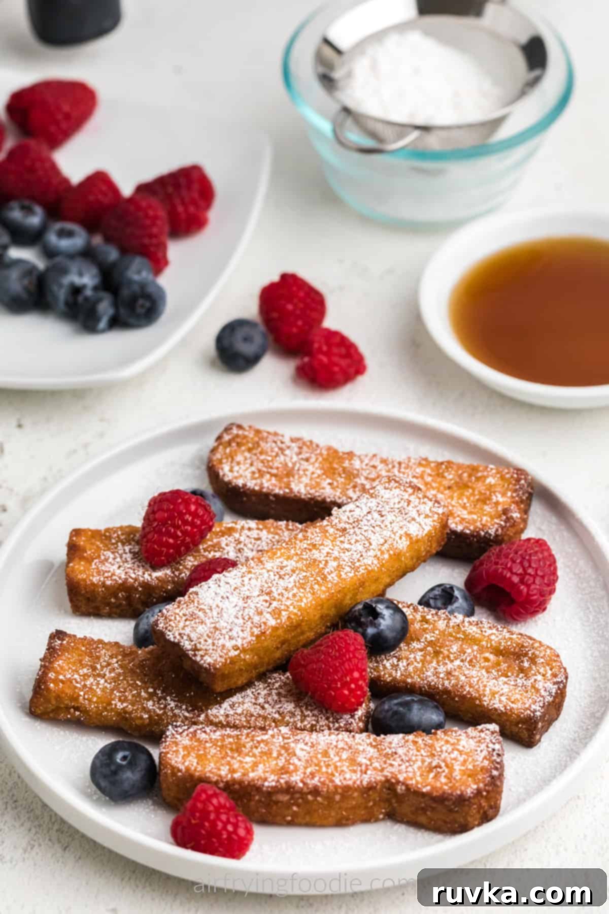 Crispy Air Fryer Frozen French Toast Sticks 7 Air fryer frozen french toast sticks fully cooked and served on a white plate with berries and powdered sugar. Ready to eat.