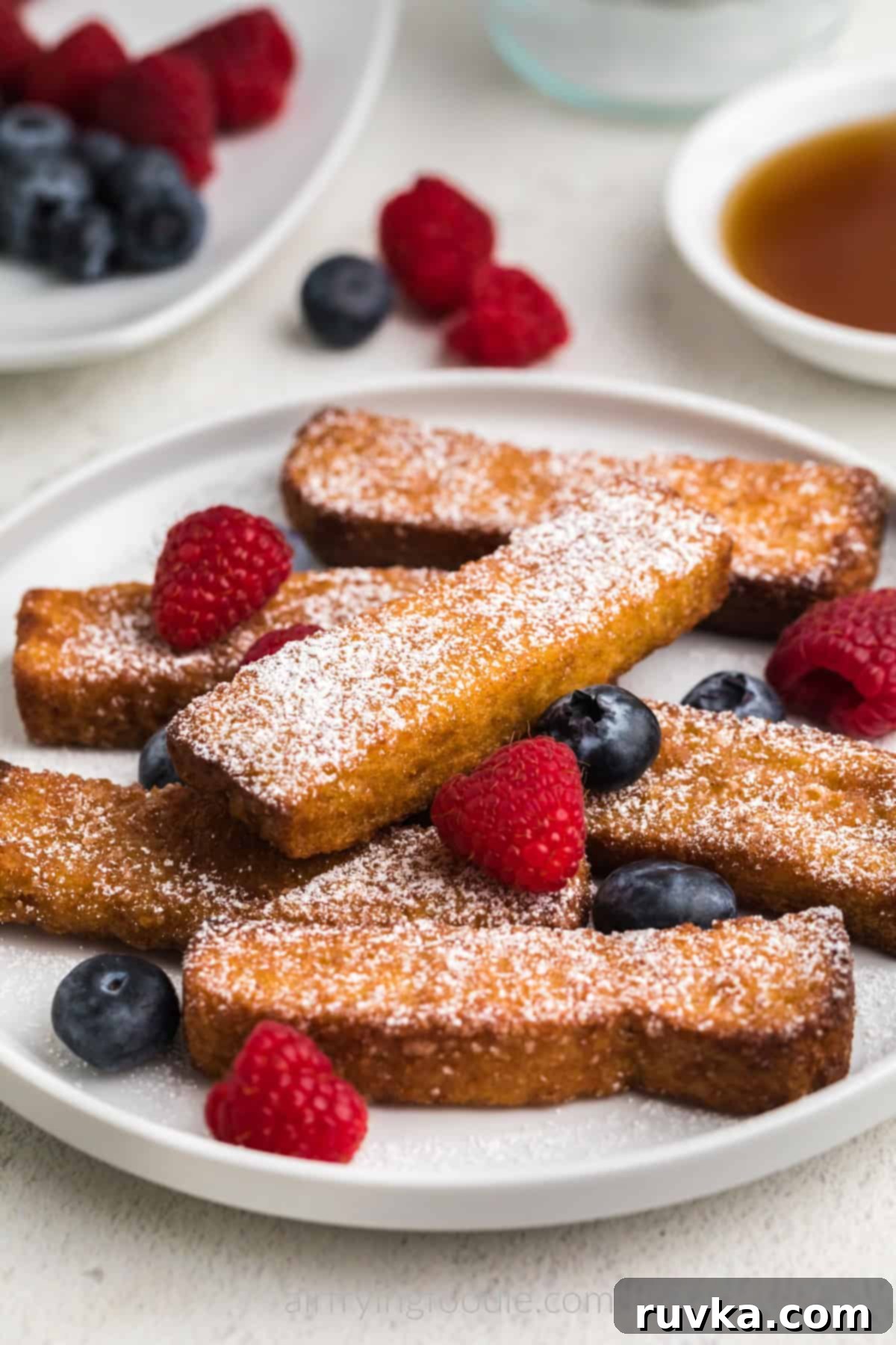 Crispy Air Fryer Frozen French Toast Sticks 8 Close up photo of air fryer frozen french toast sticks on a white plate with powdered sugar and berries.