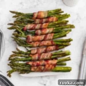 Crispy Air Fryer Bacon Wrapped Asparagus 7 Golden brown crispy bacon wrapped around asparagus stalks on a white rectangle plate.